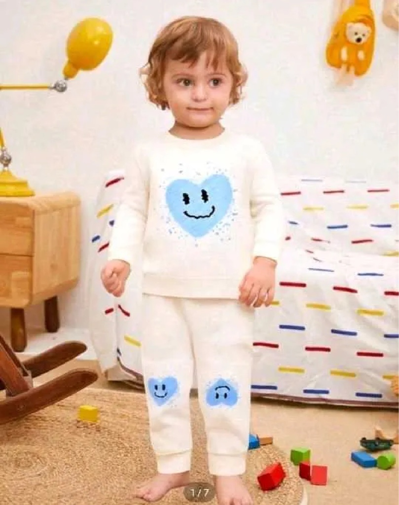 Este conjunto de ropa blanca para bebé de la marca Adrykids presenta un estampado de corazón azul con cara sonriente en el pecho.