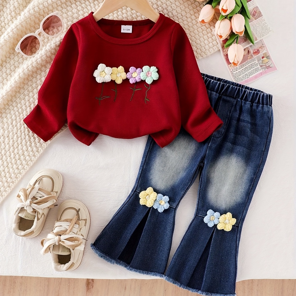 Este adorable conjunto infantil de dos piezas para niña presenta una blusa rojo vino de manga larga con textura tipo waffle y detalles de flores bordadas, combinada con un pantalón de mezclilla