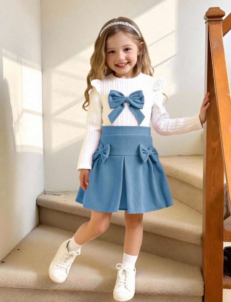 Este conjunto de ropa infantil de SHEIN incluye un top blanco de manga larga con lazo azul y una falda plisada de pana azul.
