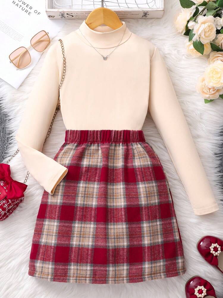Este conjunto infantil de SHEIN presenta una blusa de manga larga en tono apricot y un short-falda con estampado de cuadros rojos.