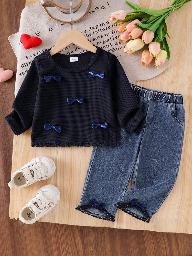 Este encantador conjunto de bebé de manga larga en color azul marino está decorado con delicados lazos tridimensionales y un sutil acabado de flecos.