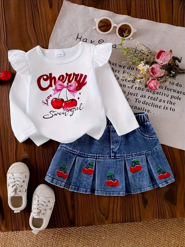 Este conjunto infantil incluye una blusa blanca de manga larga con volantes y bordados de cerezas en la falda vaquera plisada.