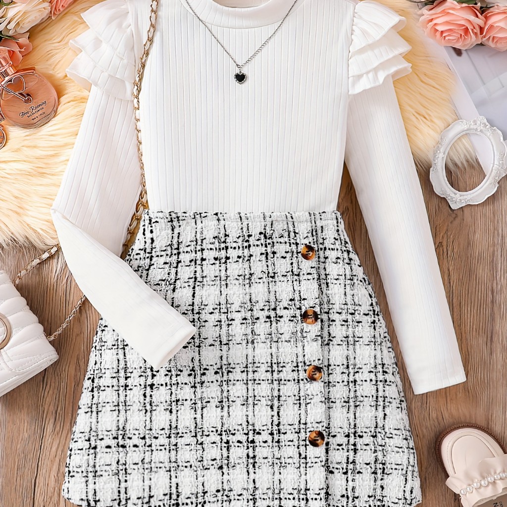 Este conjunto infantil de 2 piezas presenta una blusa blanca de manga larga con volantes y una falda de cuadros estilo Tweed con botones.