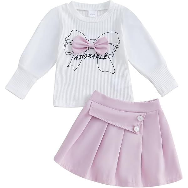 Este conjunto de ropa para niña presenta una blusa blanca de manga larga con detalles abullonados y un estampado de lazo, combinado con una falda rosa.