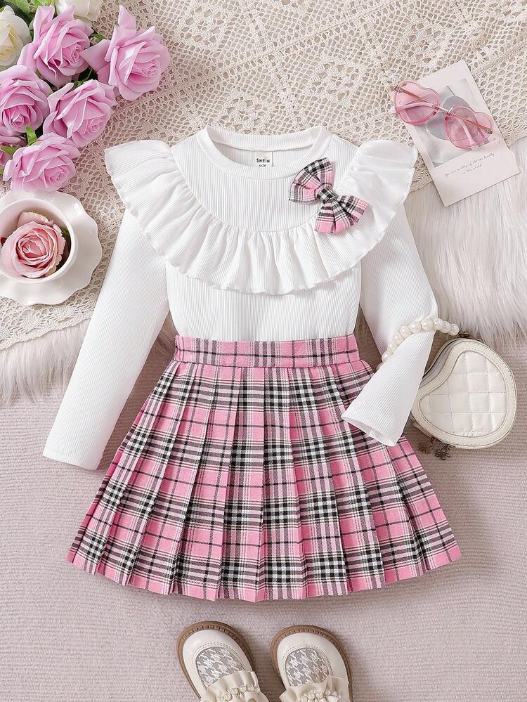 Este hermosos conjunto de falta y blusa de manga larga blanca para niña destaca por su delicado cuello con volantes y un tierno lazo decorativo de cuadros rosados.